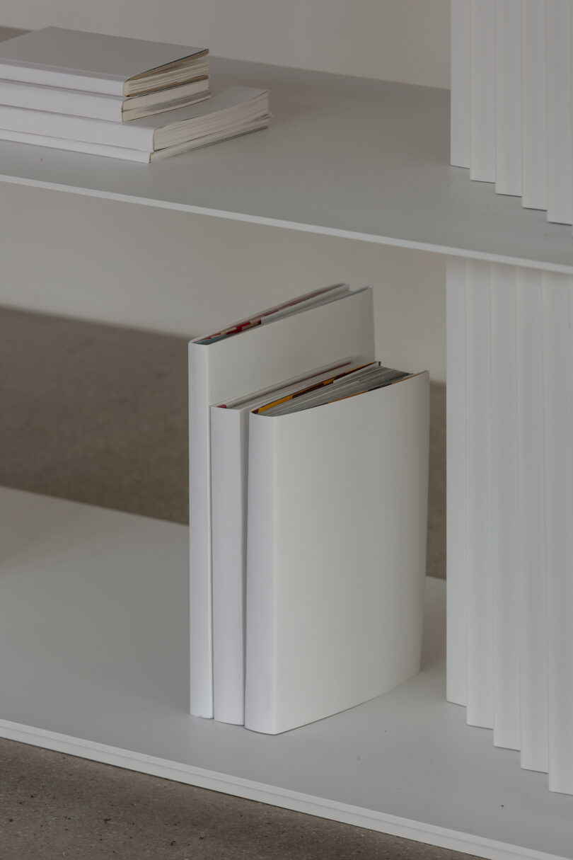 White books with blank covers are displayed on a white shelf