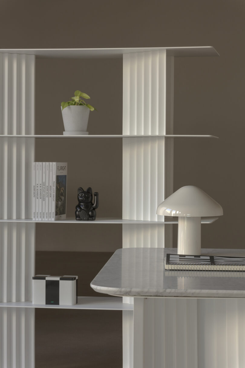 White shelving unit with a potted plant, books, a black cat figurine, and a white lamp on a marble surface