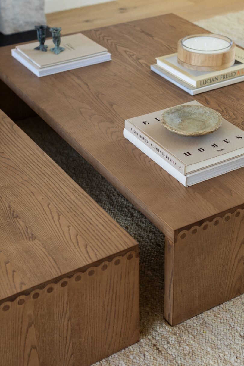 A wooden coffee table with stacked books, a ceramic plate, and two decorative figurines on top.