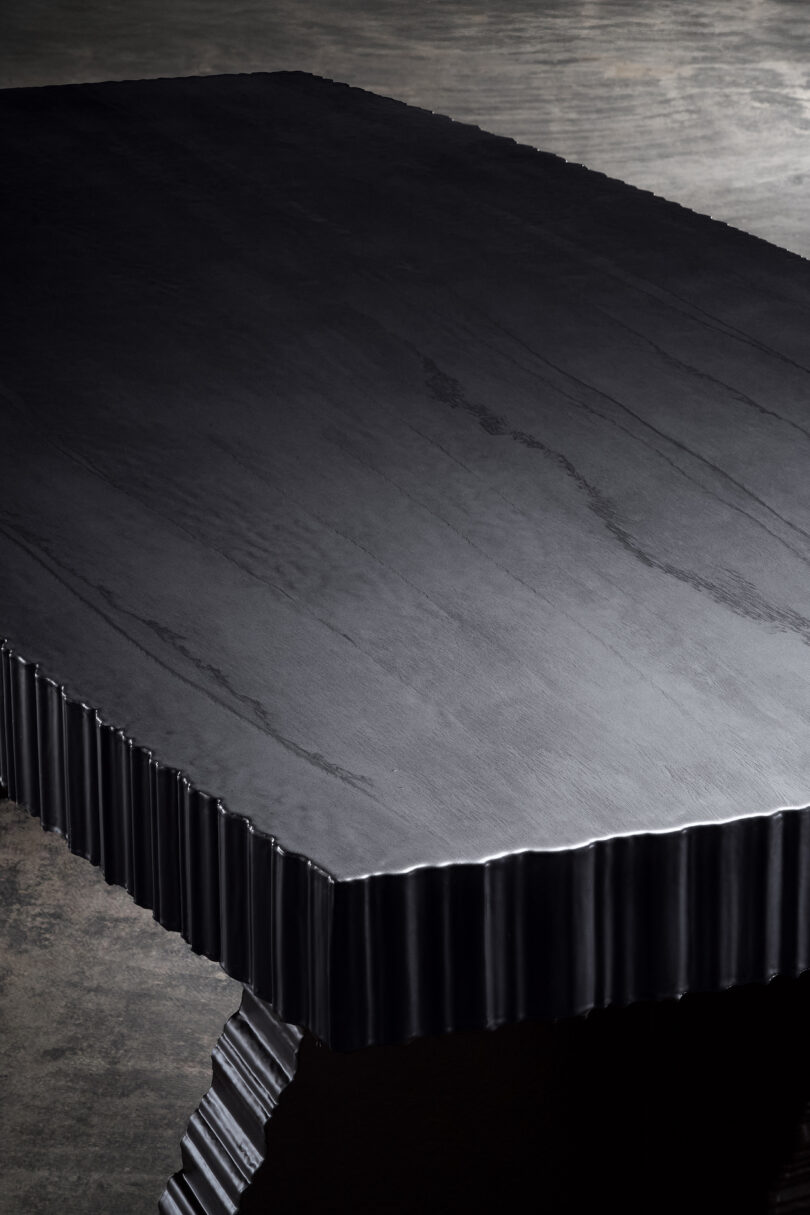 Close-up of a dark, textured table with a jagged edge, set against a plain, muted gray background