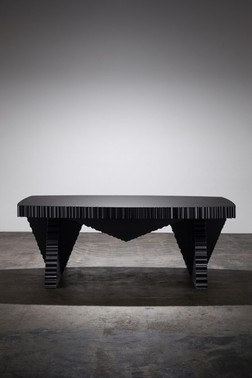 A modern black table with geometric legs and texture, set against a plain, neutral background