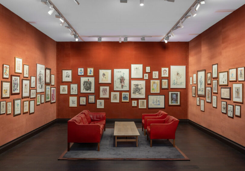 Room with red fabric walls and dozens of framed drawings