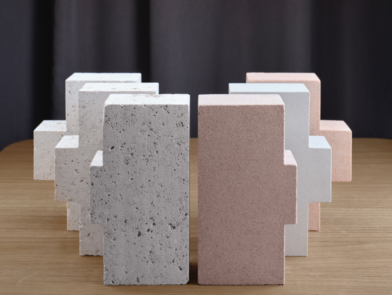 Geometric blocks of natural stone and pastel concrete bricks arranged in alternating patterns on a wood table.
