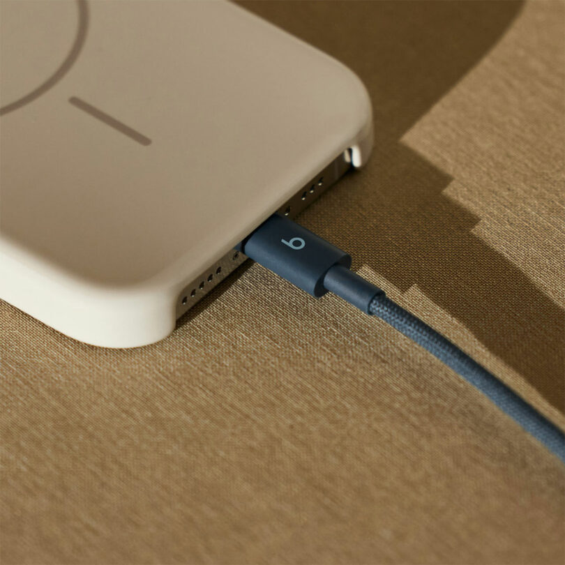 A phone in a beige case, connected to a blue Beats charging cable, rests on a brown textured surface.