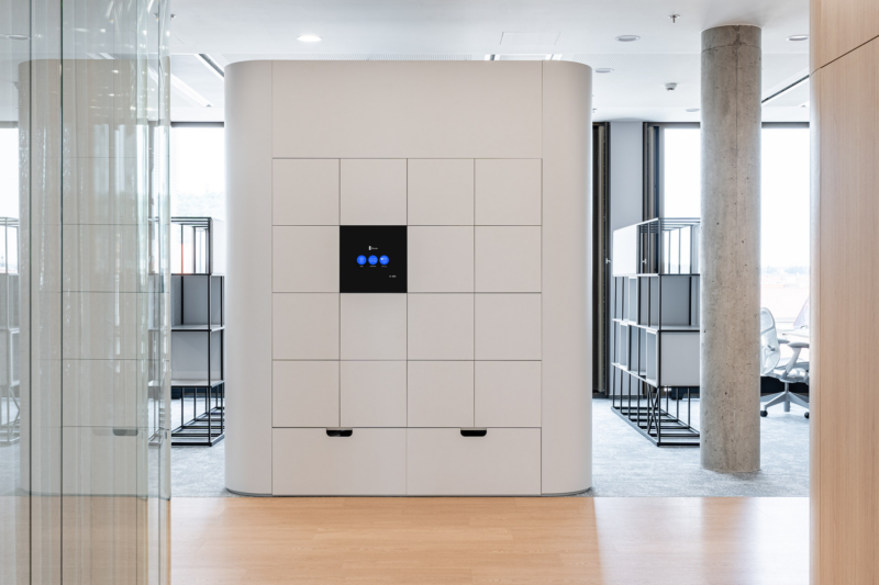 Sleek, modern smart locker unit with digital touch screen in a minimalist office hallway.