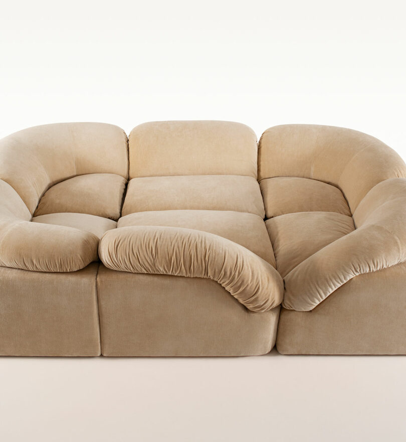 A large, beige, modular sofa inspired by Faye Toogood, featuring plush, rounded cushions and a low profile, arranged in a square shape on a plain background.