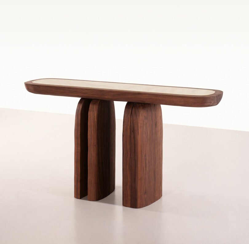A wooden console table inspired by Faye Toogood, featuring a rectangular top and three wide, rounded vertical legs, placed against a plain white background.