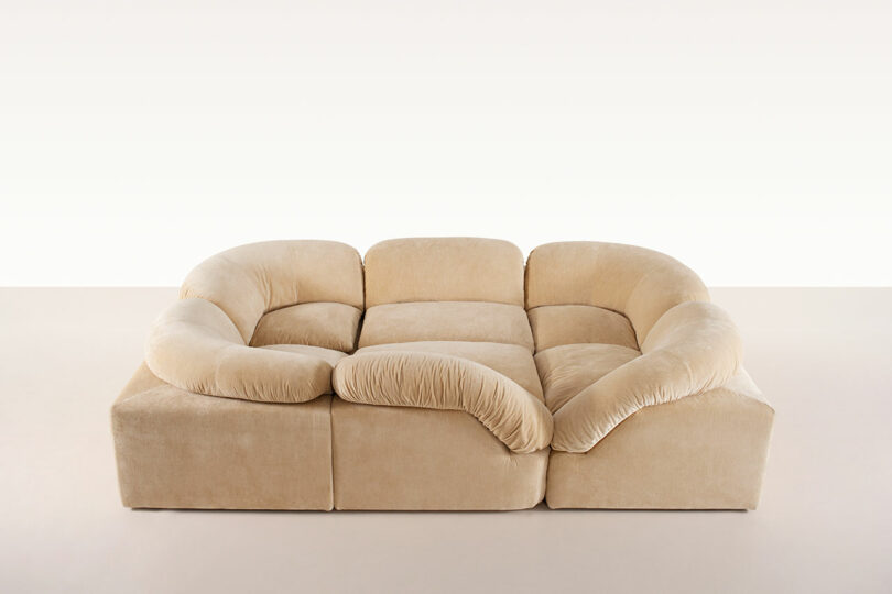 A beige, modular sofa inspired by Faye Toogood features plush, curved back and armrests, set against a plain, light background.