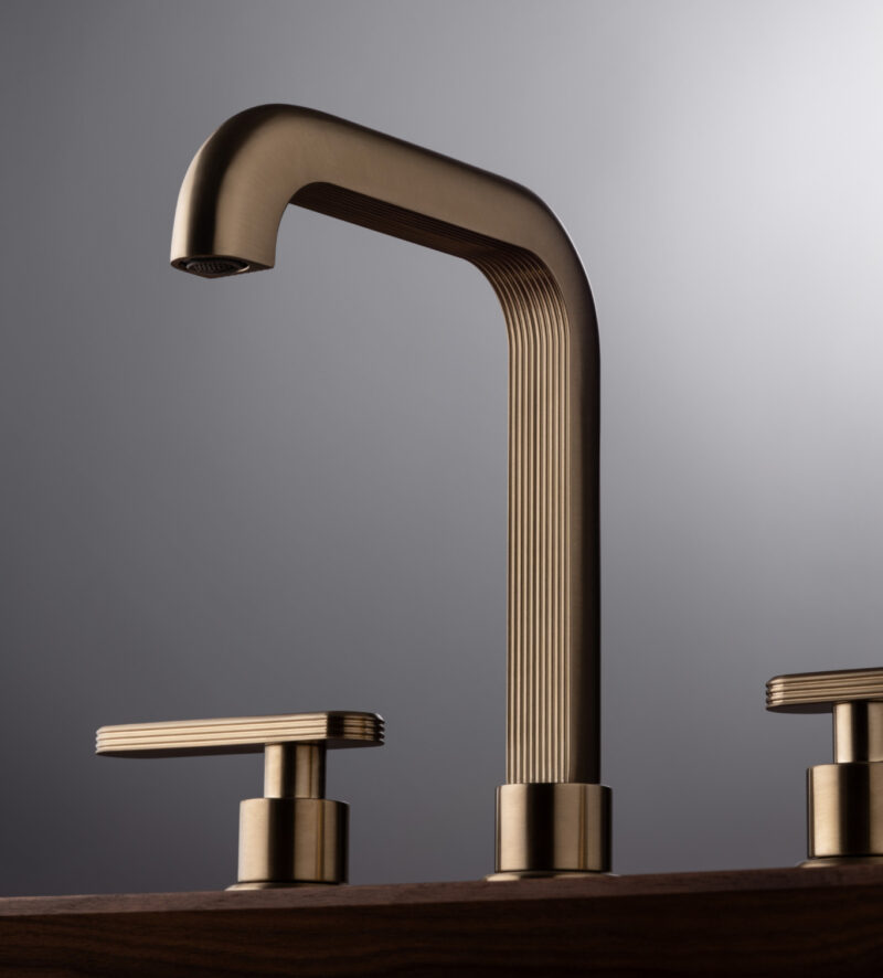 Close-up of a luxury faucet in brushed brass with ribbed detailing, set against a muted grey backdrop.