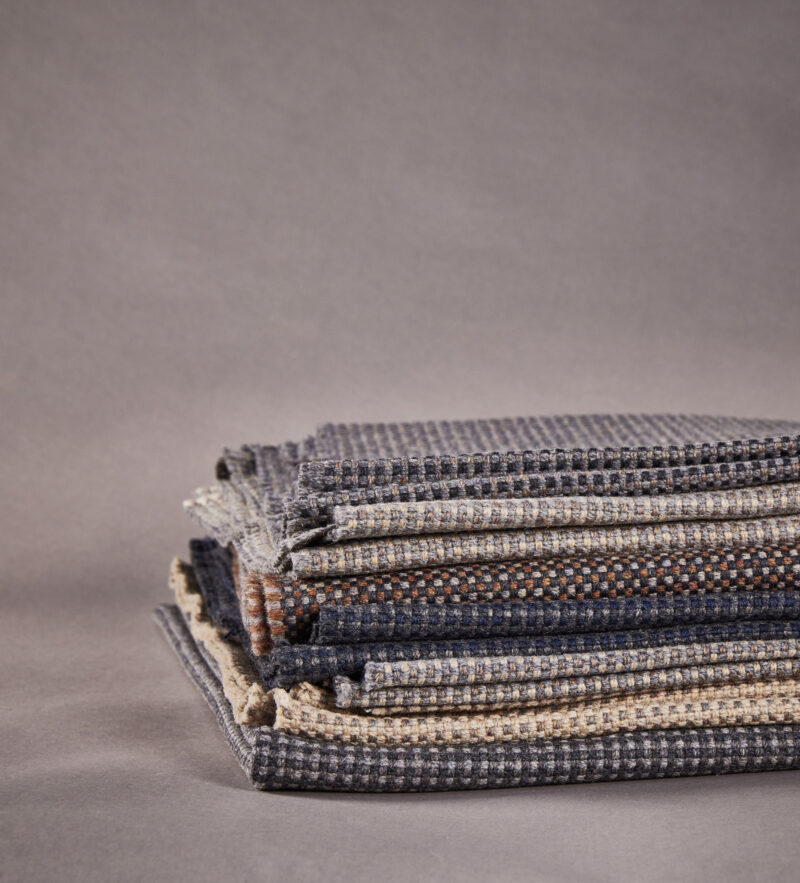 Folded stack of textured wool fabric swatches in neutral tones with subtle patterns.
