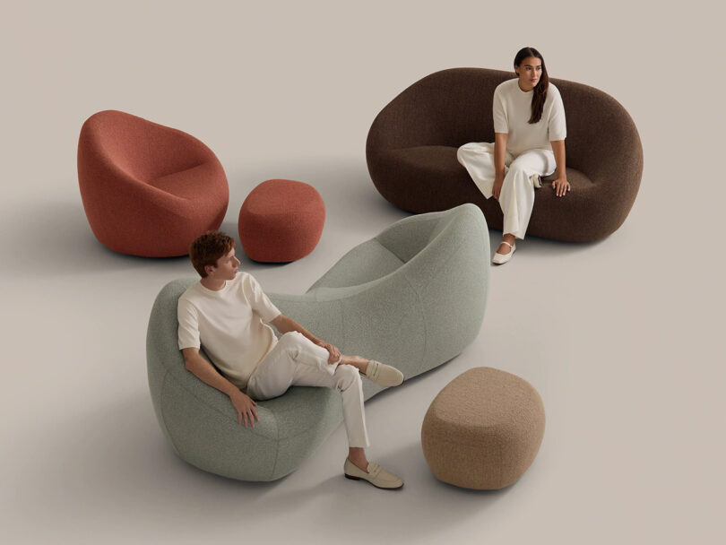 Two people sit on modern, curved sofas in muted colors, surrounded by matching poufs, against a plain, neutral background.
