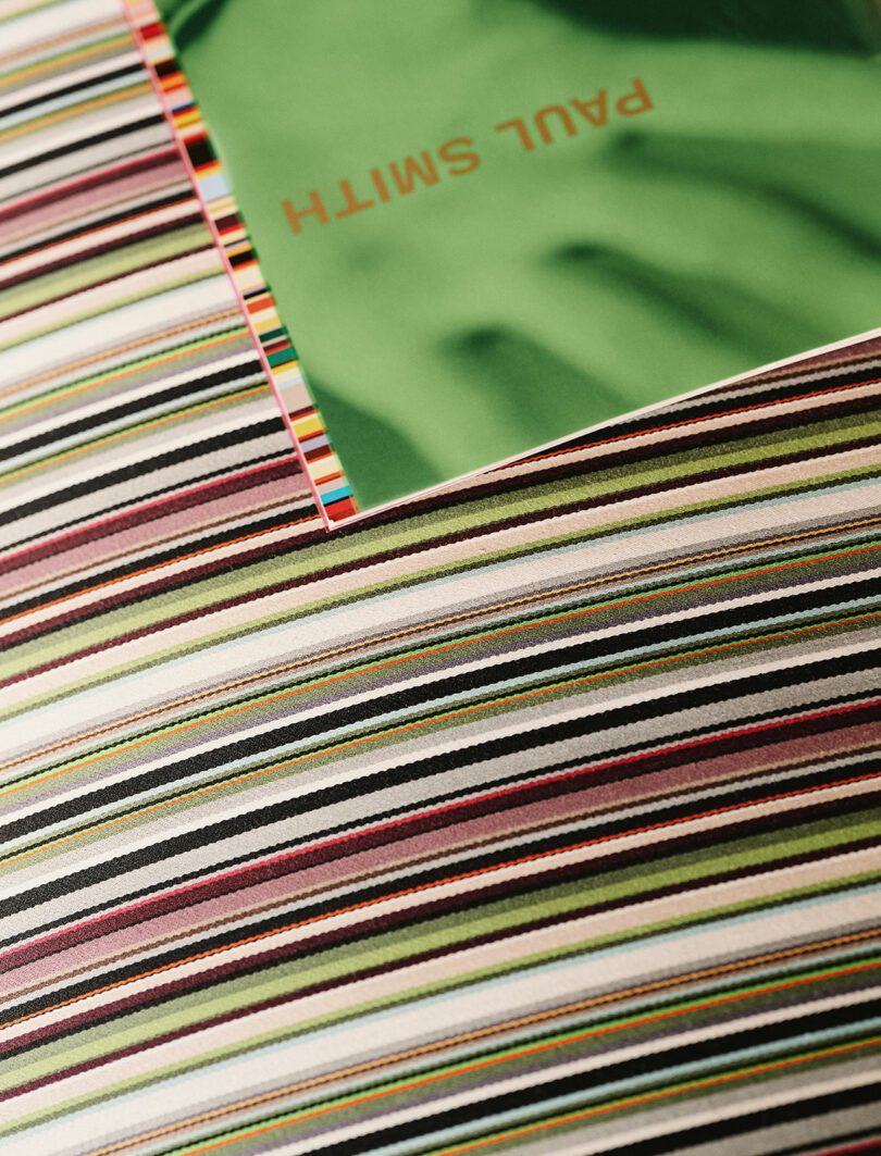 A green booklet with "PAUL SMITH" written on it rests on a multicolored striped fabric surface.