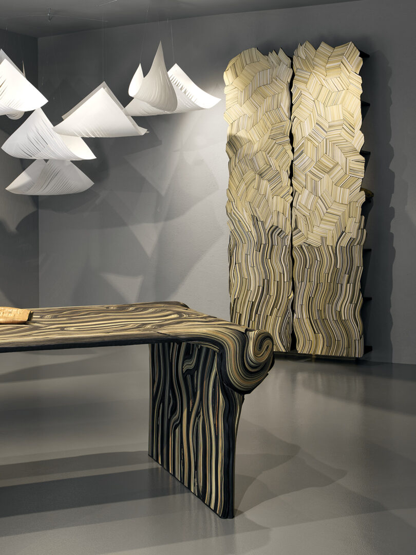A modern interior features a sculptural woodgrain-style desk, a matching textured cabinet, and geometric white hanging light fixtures.