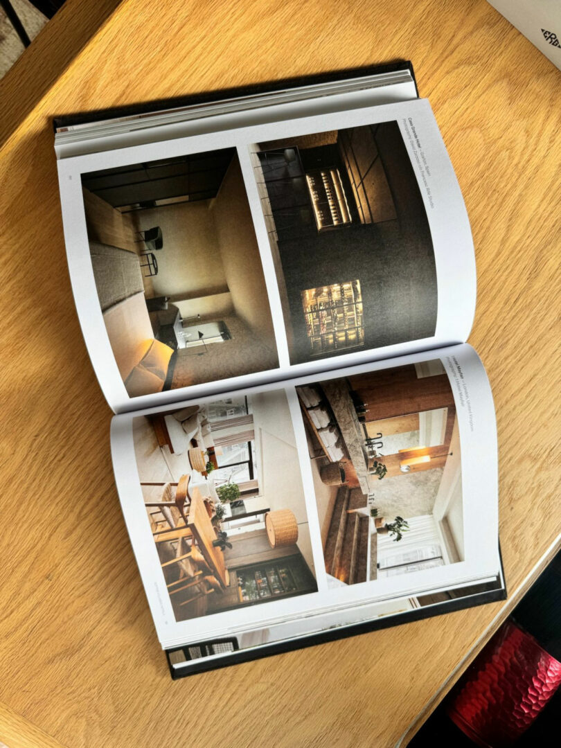 An open book on a wooden table displays four photographs of modern, minimalist interior spaces, including living and dining areas styled with Neil Ferrier’s signature aesthetic.