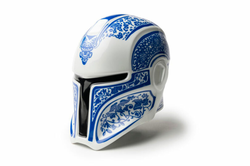 A white Mandalorian-style helmet with blue decorative patterns and black visor details, this piece channels Neil Ferrier’s flair, resembling intricate ceramic or porcelain designs.