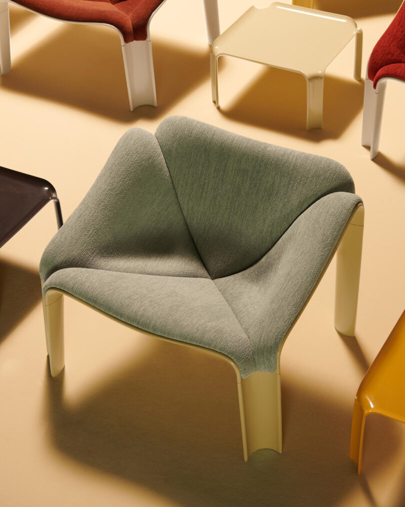 A modern lounge chair with a light green upholstered seat and cream-colored legs, surrounded by several low, rectangular tables in various colors.