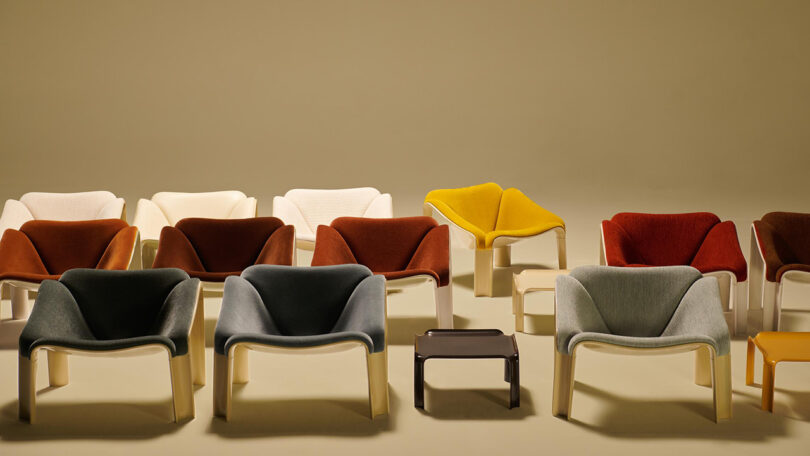 A group of modern lounge chairs in various colors, including grey, white, orange, red, and yellow, arranged in rows with two small tables in front.