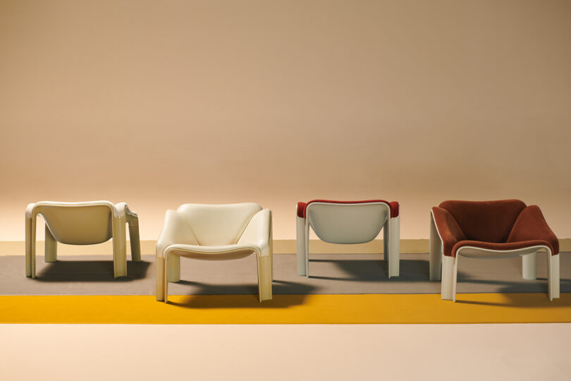 Four modern lounge chairs in white and rust colors are arranged in a row on a floor with gray and yellow stripes, against a beige background.