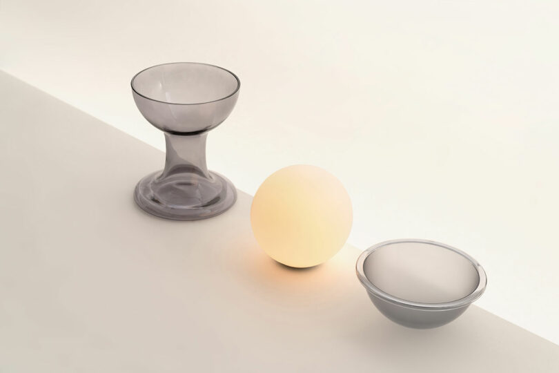 Three objects on a light surface: a translucent glass cup, a glowing Gelato Lamp by Carlo Nason in the center, and a shallow glass bowl on the right.