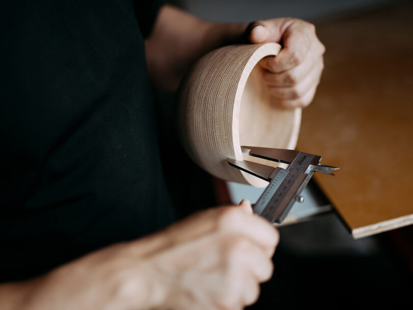 A person uses a caliper to measure the inner diameter of a wooden bowl while holding it in one hand.