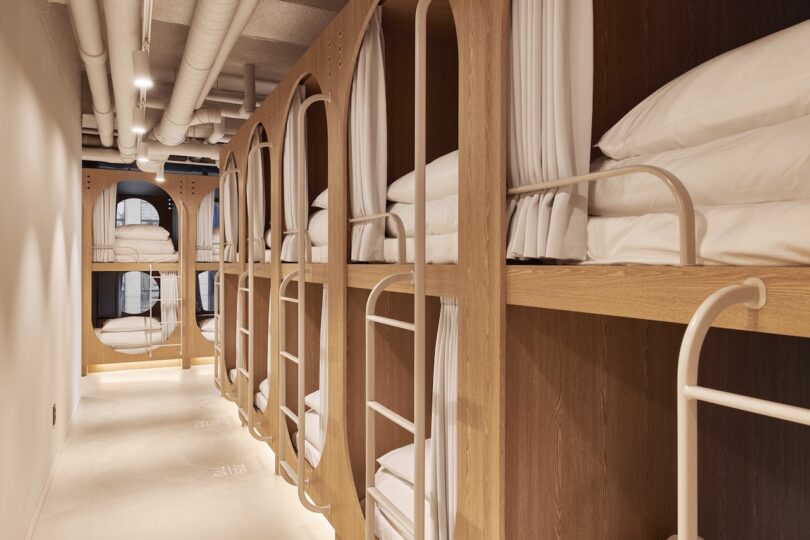A hall lined with wooden beds, each with white bed linen, privacy curtains and stairs, offers an elegant capsule style at the Drip & Drop hotel