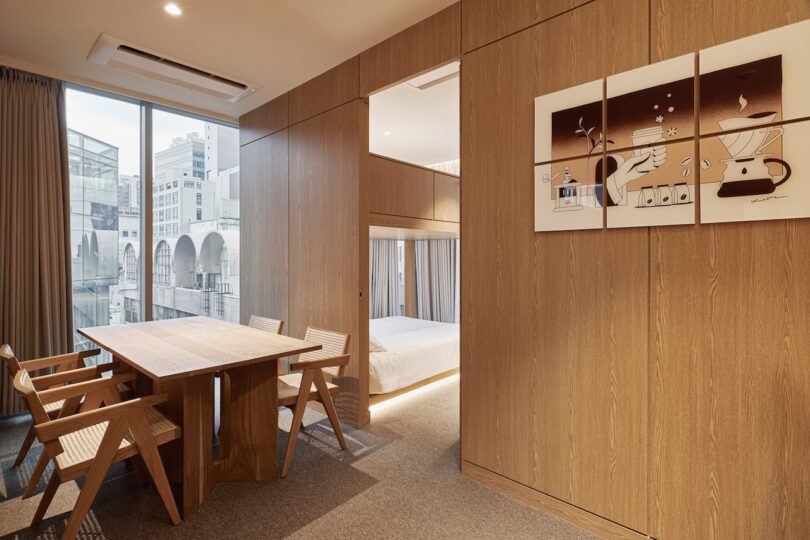 Modern hotel suites with wooden panels, a table for four, large window, partial view in bedroom and art with coffee theme framed on the wall