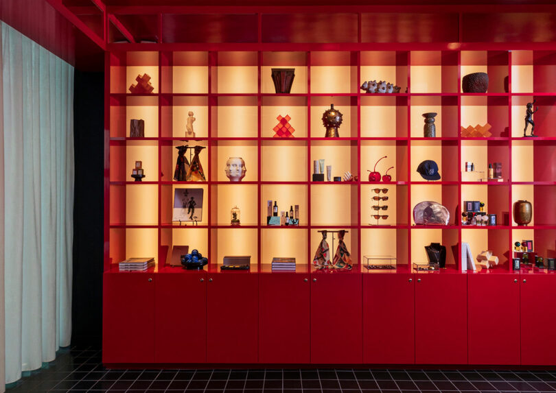 A red shelving unit with illuminated square cubbies displays various decorative objects, books, and sculptures against a softly lit backdrop.
