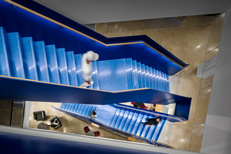 Overhead view of a modern blue staircase in a building, with several people walking and sitting in surrounding lounge areas.