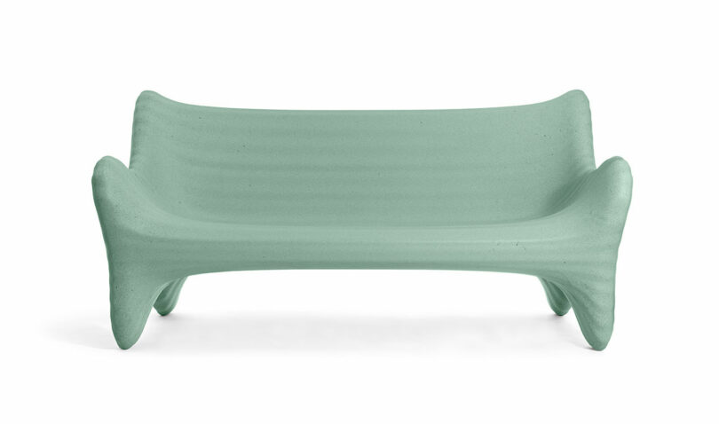A modern, light green loveseat with smooth, curved lines and sculptural armrests, inspired by the In-Side Thomas Heatherwick design ethos, displayed against a plain white background.