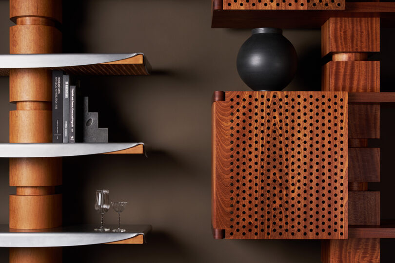 Modern wooden shelves with books, two glasses, and a decorative black vase against a dark wall; right shelf features a perforated wooden panel design.