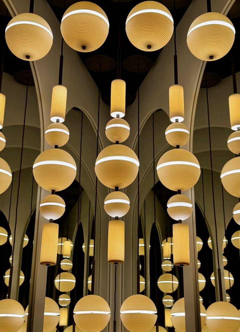 Hanging round and cylindrical Lee Broom pendant lights are reflected in large mirrors, creating a pattern of repeating illuminated shapes.