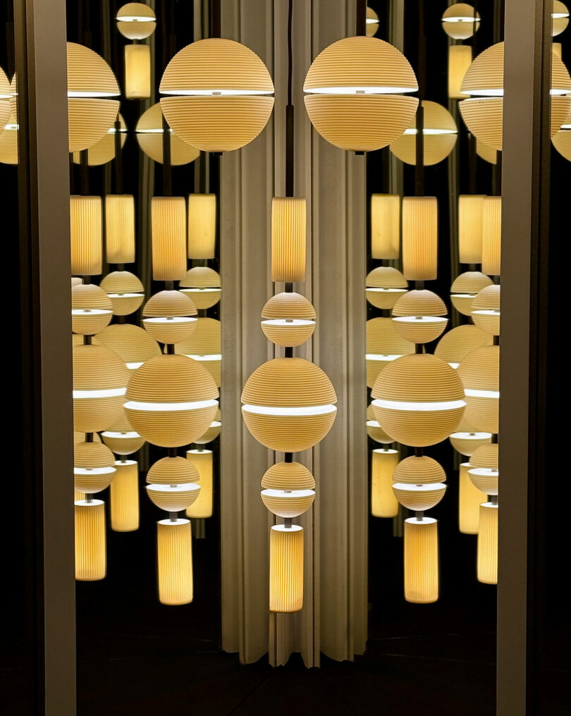 A group of round and cylindrical yellow Lee Broom lamps are reflected in mirrors, creating a repeating geometric pattern with warm lighting.