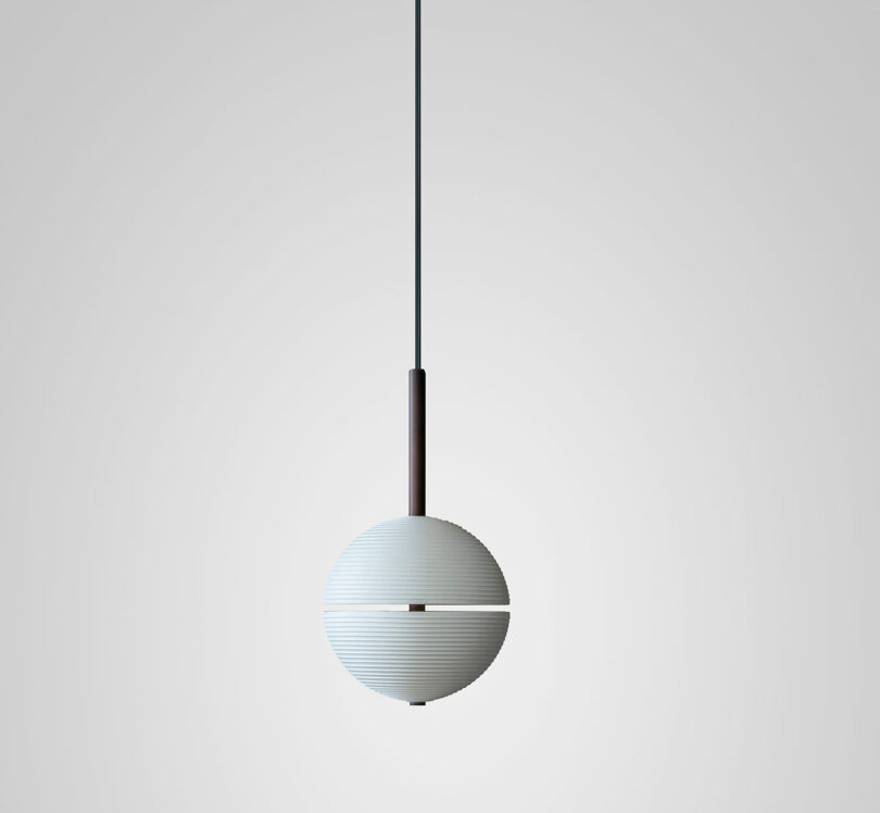 A modern, spherical pendant light by Lee Broom hangs from the ceiling against a plain, light gray background.