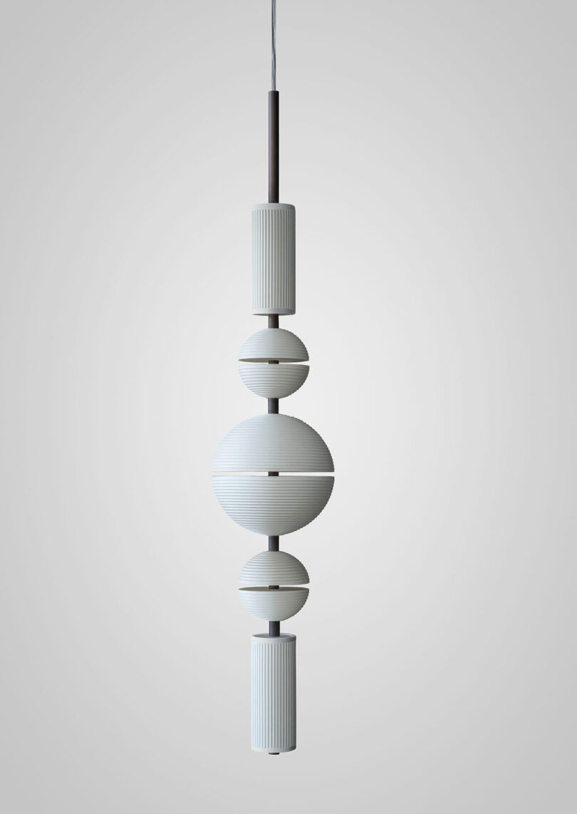A modern Lee Broom pendant light featuring a vertical arrangement of ribbed cylindrical and spherical white elements, elegantly suspended from a cord against a plain background.
