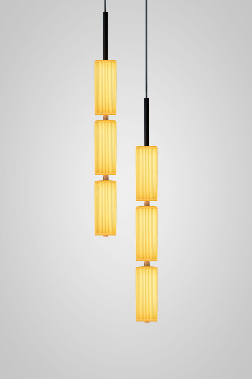 Two pendant lights with vertical, cylindrical, ribbed yellow lampshades inspired by Lee Broom hang from the ceiling against a plain light gray background.