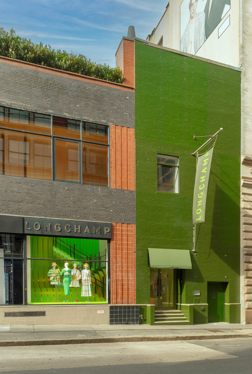 Street view of a Longchamp store with green and brick exterior, displaying mannequins in the window and a green Longchamp banner above the entrance.