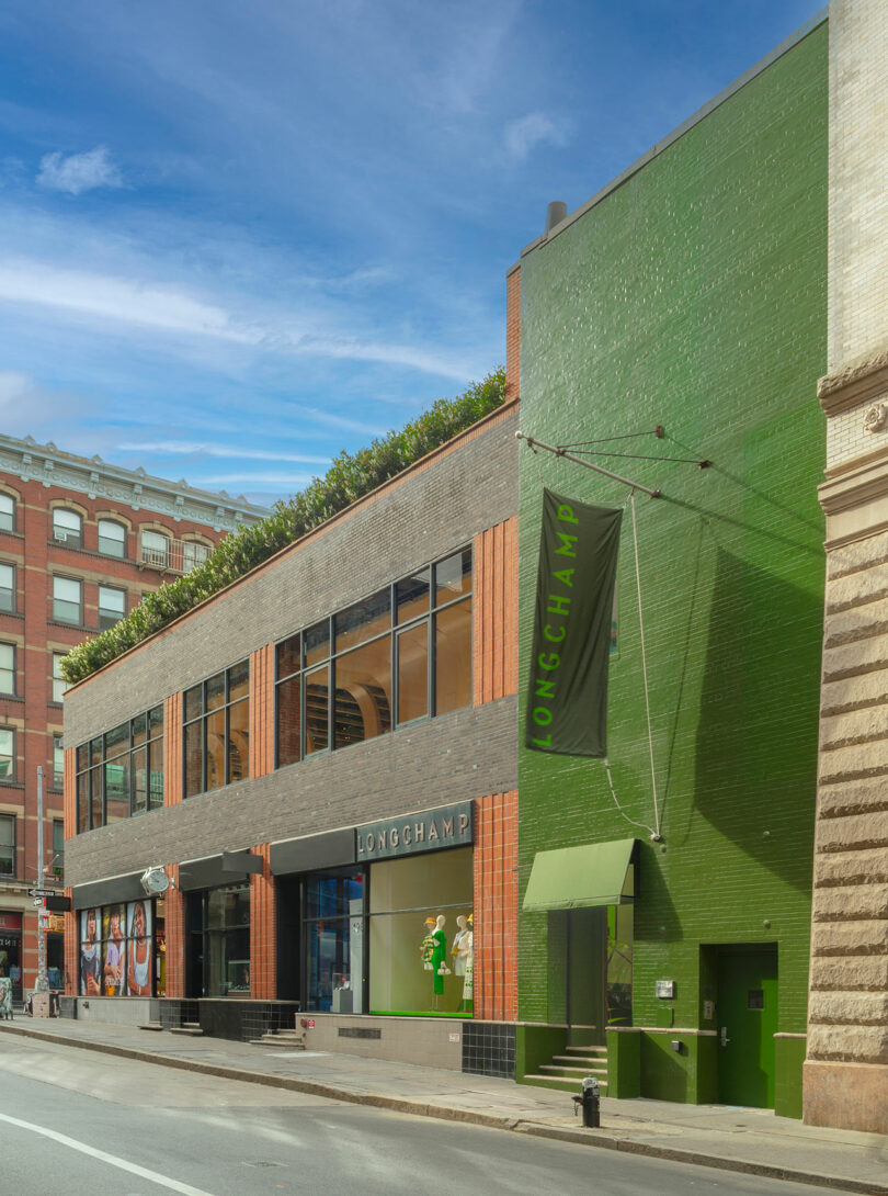 A two-story building with a green brick facade and large windows houses a Longchamp store; a green Longchamp sign hangs above the entrance.