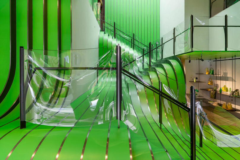 A modern interior with bright green curved walls, transparent glass barriers, and shelves displaying yellow handbags on the right side.
