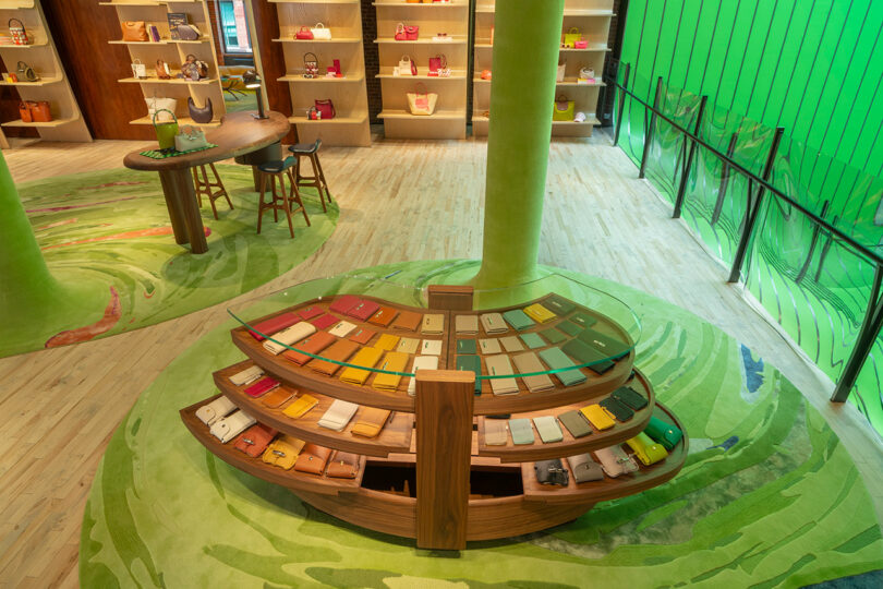 A retail store interior with shelves and display tables showcasing colorful handbags and wallets, set against green walls and wood flooring.
