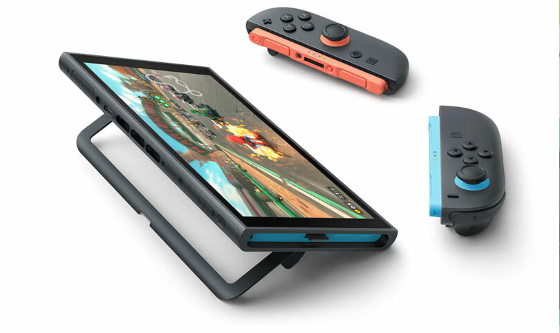 A tablet-like gaming console, resembling a Switch 2, displays a racing game on screen as it’s propped on a stand, with two detachable controllers placed nearby.