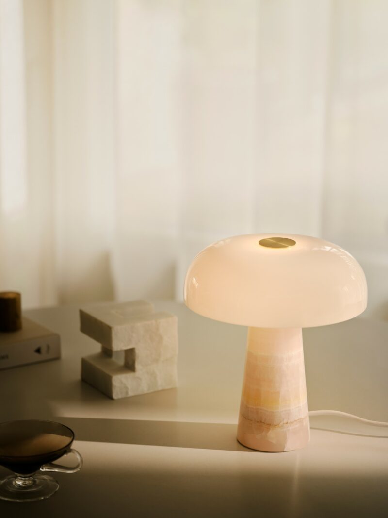 Softly glowing mushroom-style table lamp with a pinkish marble base on a minimalist desk.