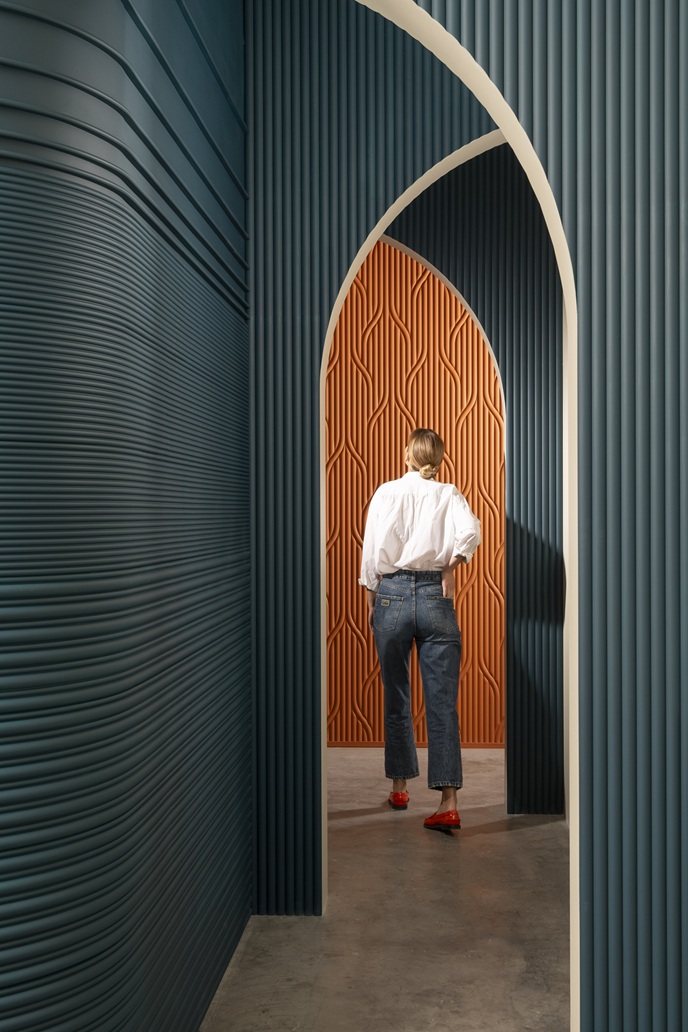 Person walking through sculptural archways clad in ribbed blue and orange wall panels.