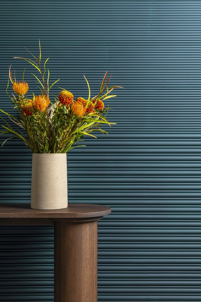 Yellow and orange flowers in a ceramic vase set against deep blue fluted wall panels.