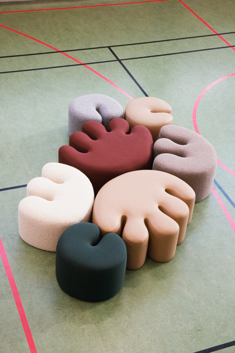 A cluster of abstract, hand-shaped and rounded upholstered seats in various colors arranged on a gymnasium floor.