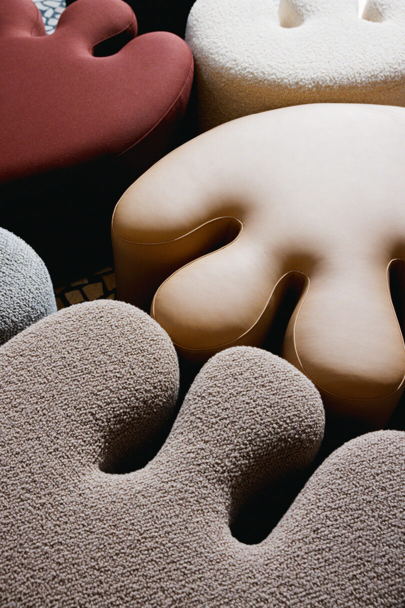 Abstract, blob-shaped upholstered seats in various neutral and earthy tones, arranged closely together on a patterned floor.
