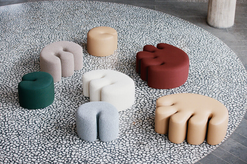 A group of colorful, uniquely shaped ottomans are arranged in a circle on a mosaic tile floor.