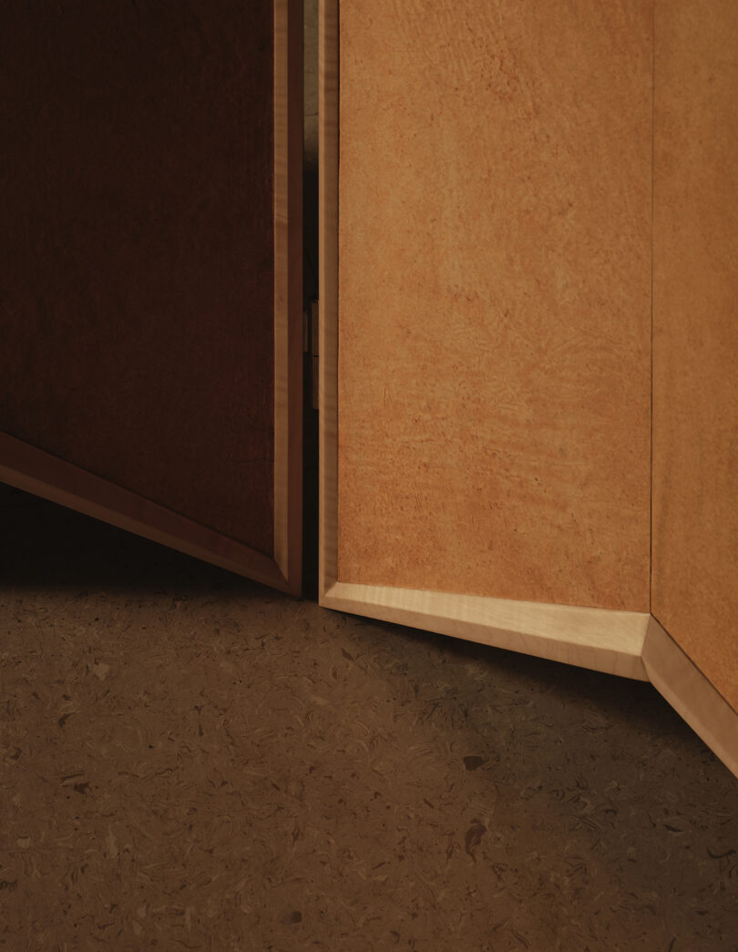 Two light-colored wooden doors are slightly open, revealing a dark interior; the floor is textured with a similar brown tone.