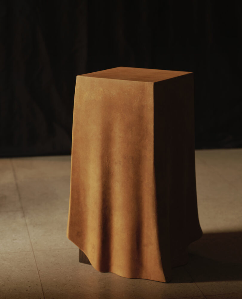 A wooden pedestal is partially draped with a cloth, standing on a tiled floor against a dark background.