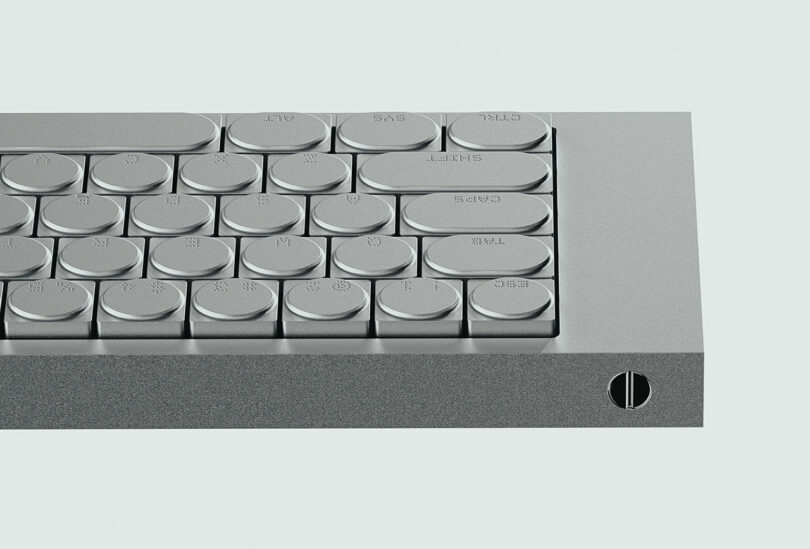 A close-up of a minimalist metallic keyboard with circular keys and a thick, flat edge featuring a single cleaver-inspired screw detail.