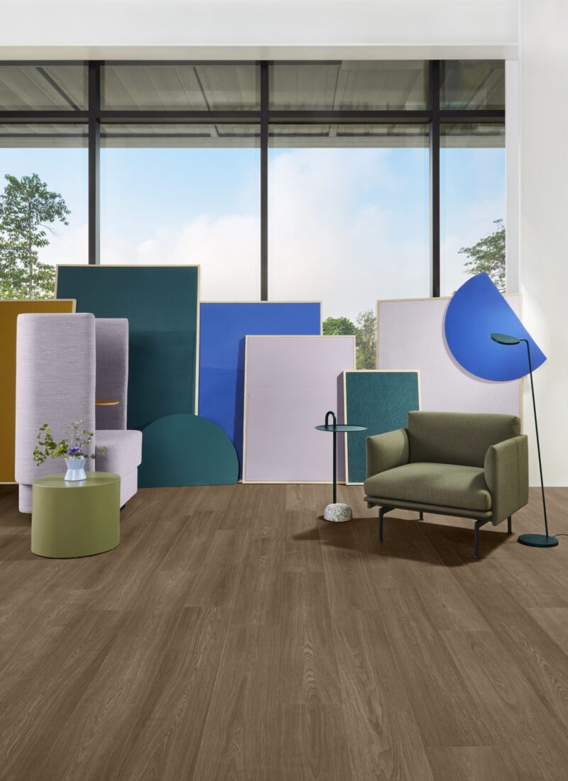 Green armchair and side tables set on wood-look flooring with colorful acoustic panels arranged behind.